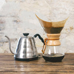photo d'une bouilloire en métal et d'une cafetière en verre Chemex contenant un filtre papier et du café